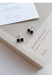 Detail of silver bow earrings with black heart zircon set against a vintage book background