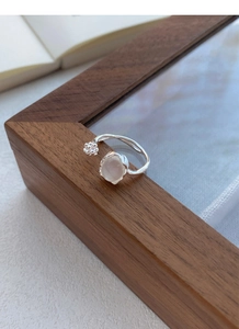 Macro shot of silver ring with white chalcedony bud and branch on a wooden edge