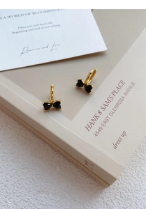 Detailed view of gold bow earrings with black heart-shaped zircons on cream book pages