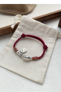 Détail du bracelet en soie rouge tressée avec breloque chat argenté et étiquette brodée Miao