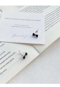 Detail of silver bow earrings with heart-shaped black stones on romantic background