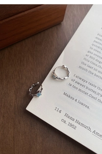 Détail de créole en argent avec zircon bleu carré posée sur un papier texte vintage