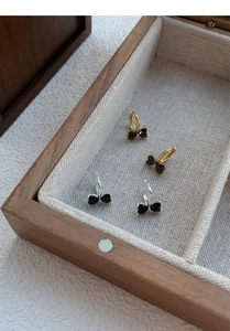 Close-up of gold and silver hoop earrings with black zircon bow pendants in a wooden box