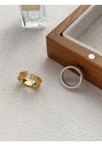 Close-up of gold cluster ring and silver zircon band on a textured background