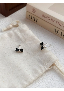Detail view of S925 sterling silver bow earrings with black heart stones on beige pouch