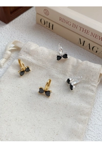 Close-up of bow-shaped heart zircon earrings in gold and silver on a linen pouch