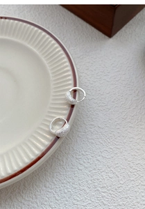 Détail de créoles en argent S925 avec texture mate sur une assiette en céramique