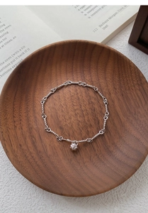 Close-up of S999 sterling silver rope chain bracelet with bell charm in a wooden bowl