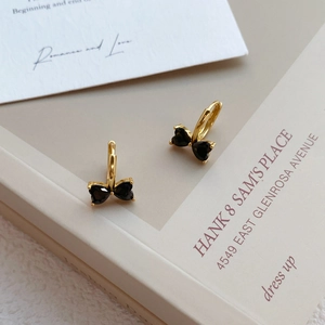 Elegant gold bow-shaped hoop earrings with black heart-shaped zircons on aesthetic book background