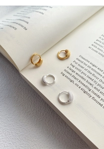 Gros plan de boucles d'oreilles S925 dorées et argentées mates posées sur un livre ouvert