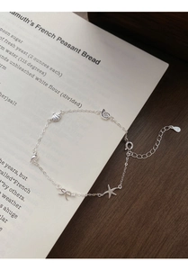 Close-up of S925 silver bracelet with starfish, shell, and bow charms on a book