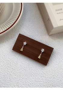 Detailed shot of star and pear-cut zircon earrings on a wooden stand in soft lighting
