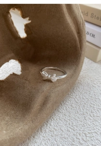 Close-up of S999 sterling silver bow ring with brushed finish on artistic backdrop