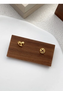 Macro detail of asymmetric S925 silver horse and coin stud earrings on wooden display