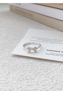 Detailed close-up of a brushed S999 silver bow ring on a white decorative display card