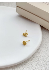 Detailed close-up of matte gold asymmetrical rocking horse and coin stud earrings on porcelain