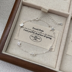 Elegant S925 silver bracelet featuring starfish, shell and bow charms on linen display