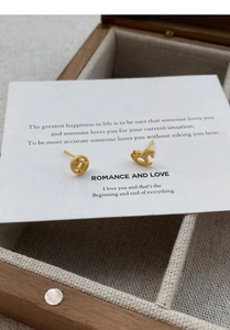 Detailed view of asymmetric matte gold horse and coin studs on an elegant display card