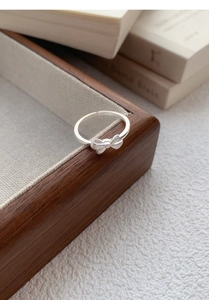 Detail of matte S999 silver bow ring on a wooden box with an adjustable open design