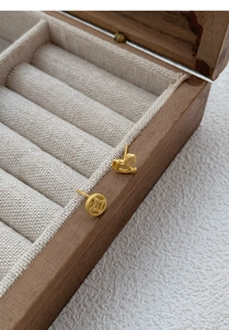Detailed macro of asymmetric gold rocking horse and coin stud earrings on wooden box