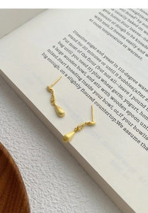 Macro shot of 18K gold plated teardrop tassel earrings on an open vintage book