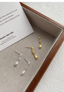 Detail of matte waterdrop tassel earrings in gold and silver finish with zircon accents