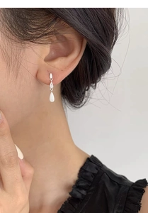 Macro view of long water drop silver earrings with zircon accents and brushed finish
