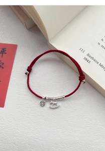 Close-up of S925 silver horse and coin charms on a red woven bracelet with peace card