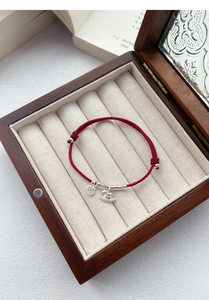 Detailed view of S925 silver horse and coin charms on a red woven cord bracelet