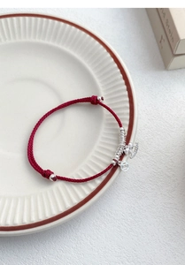 Detail of red woven S925 silver bracelet with lucky coin charm on white ceramic plate