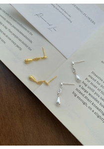 Detail of brushed gold and silver teardrop earrings with zircon on a vintage book