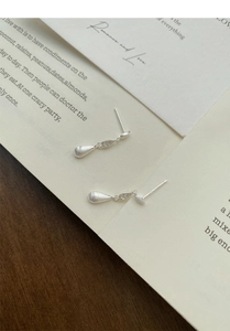 Close-up of matte brushed silver teardrop earrings with zircon accents on vintage paper