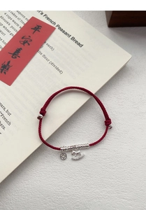 Detailed view of red woven cord bracelet with silver lucky coin and rocking horse charms