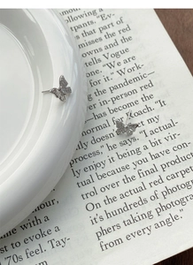 Detail of silver butterfly stud earrings with sparkling zircons on a white ceramic edge