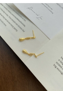 Macro shot of matte gold drop earrings with zircon on vintage book pages and wood