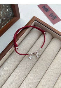 Detail of red braided cord bracelet with silver money coin and hollow rocking horse charms