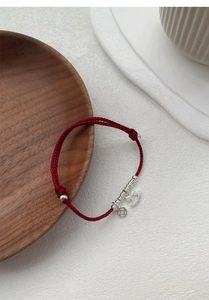 Detailed macro of a red braided cord bracelet with silver coin and crown charms on wood