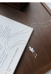 Dettaglio della collana con fiori di gardenia d'argento e nappe su legno scuro