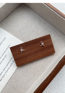 Close-up of S999 silver fishtail stud earrings with a sparkling zircon on a wood tray