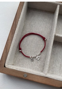 Detail of red braided string bracelet with S925 silver coin and elephant charms