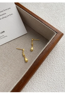 Close-up of matte gold teardrop earrings with zircon accents on a neutral base