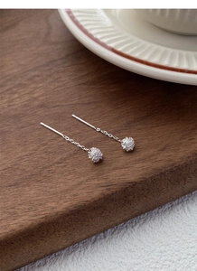 Macro shot of S925 sterling silver dandelion tassel earrings on dark wood surface