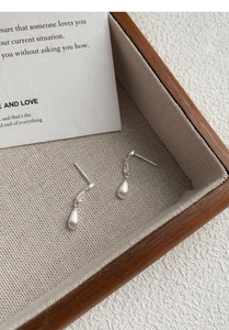 Macro shot of brushed silver teardrop earrings with zircon accents in a wooden tray