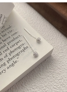 Macro detail of silver dandelion tassel drop earrings on an open book page