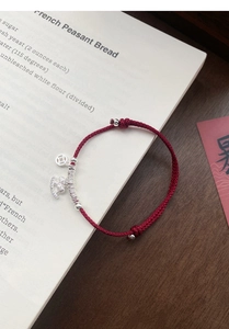 Macro detail of red woven silk cord bracelet with silver coin and logo charms