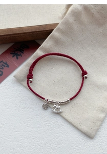 Close-up of S925 silver horse and coin charms on a red woven adjustable rope bracelet