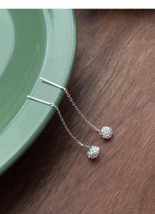 Detail of silver dandelion tassel drop earrings hanging on a green ceramic plate rim