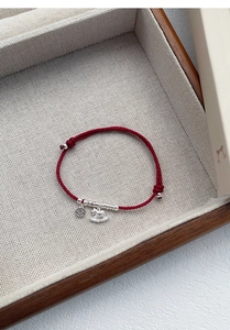 Macro shot of S925 silver horse and coin charms on a red woven bracelet in a wooden tray