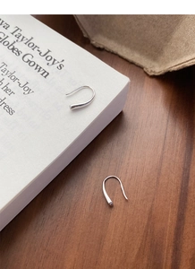 Detailed close-up of U-shaped S999 sterling silver teardrop earrings on a wooden desk