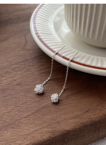 Macro detail of S925 sterling silver dandelion tassel earrings on a cream ceramic cup